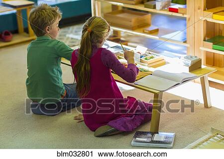 Stock Image - Caucasian children at table in classroom. Fotosearch