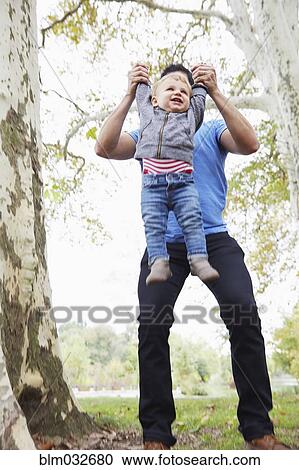 Stock Image - Caucasian father playing with baby son outdoors. Fotosearch