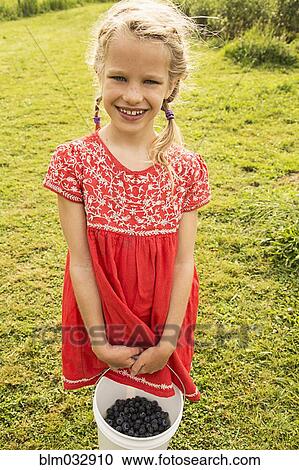 Stock Image - Caucasian girl holding basket of blueberries. Fotosearch
