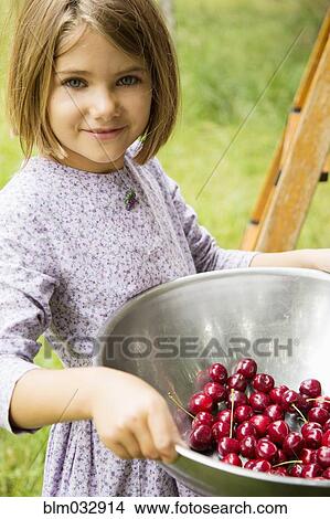 Picture - Caucasian girl holding bowl of fresh cherries on farm. Fotosearch