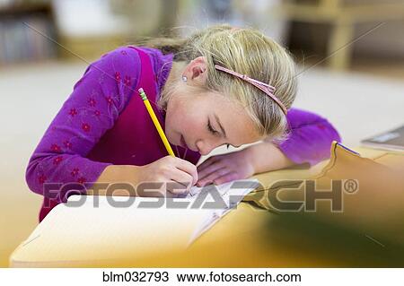 Stock Image - Caucasian girl writing in classroom. Fotosearch