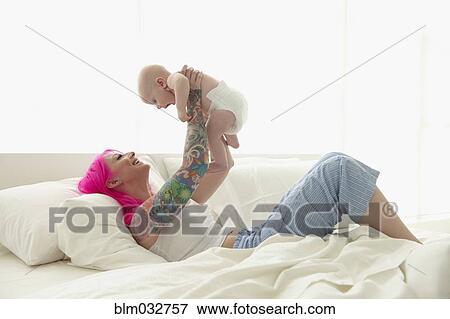 Stock Photo - Caucasian mother with pink hair and tattoos playing with baby. Fotosearch
