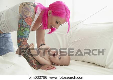 Caucasian mother with pink hair and tattoos playing with baby View Large Photo Image Stock Photograph - Caucasian mother with pink hair and tattoos playing with baby. Fotosearch
