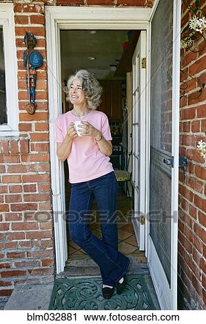 Stock Image - Caucasian woman drinking cup of coffee in doorway. Fotosearch
