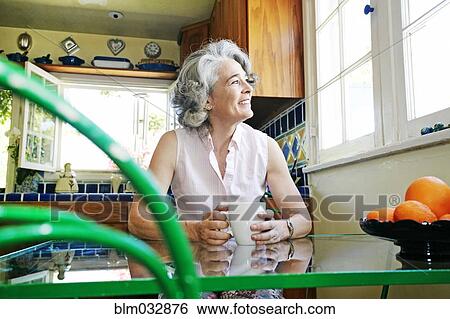 Stock Photograph - Caucasian woman drinking cup of coffee in kitchen. Fotosearch