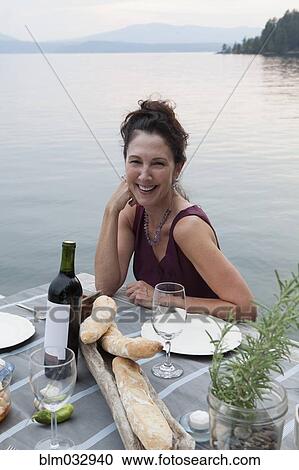 Stock Image - Caucasian woman smiling at table near lake. Fotosearch