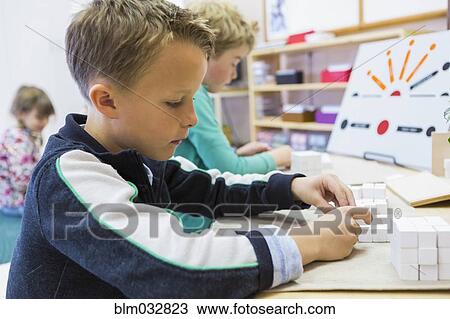 Stock Image - Close up of boy solving puzzle in classroom. Fotosearch