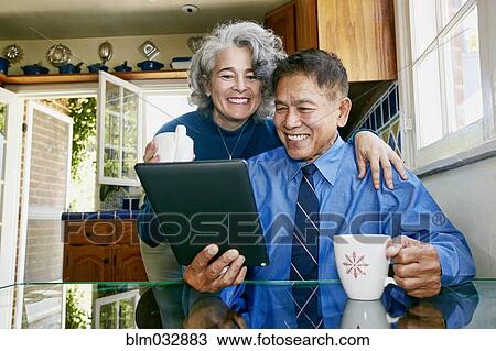 Stock Image - Couple using digital tablet in kitchen. Fotosearch