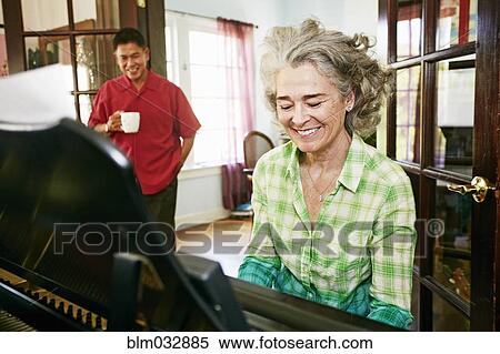 Stock Photography - Man watching wife play piano in living room. Fotosearch