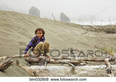 Mixed race boy crouching on driftwood on beach View Large Photo Image Stock Photo - Mixed race boy crouching on driftwood on beach. Fotosearch
