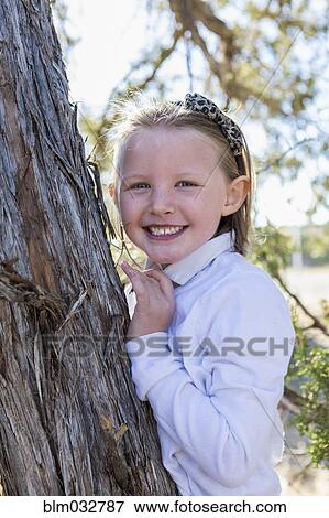 Stock Photo - Mixed race girl smiling near tree outdoors. Fotosearch