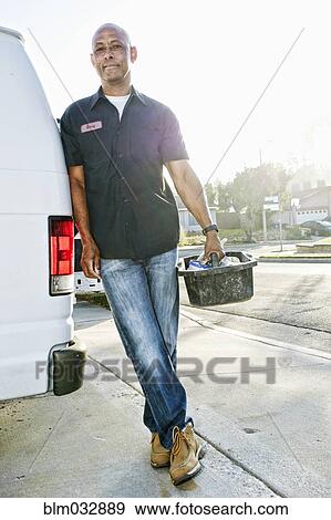 Stock Photo - Mixed race plumber holding tools van. Fotosearch