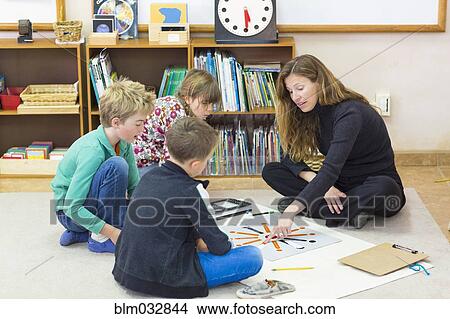 Montessori teacher helping students in classroom View Large Photo Image Picture - Montessori teacher helping students in classroom. Fotosearch