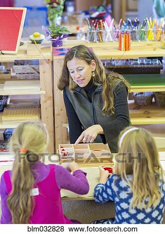 Stock Photo - Montessori teacher helping students in classroom. Fotosearch