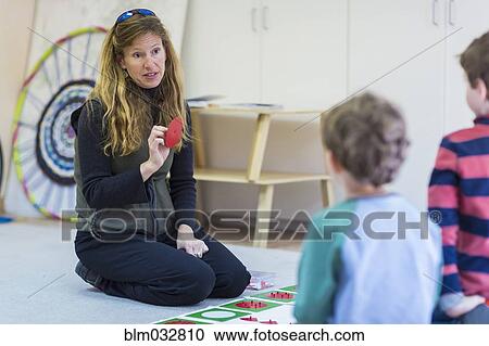 Stock Image - Montessori teacher talking to students in classroom. Fotosearch