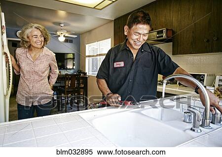 Stock Photography - Plumber testing sink for woman in kitchen. Fotosearch