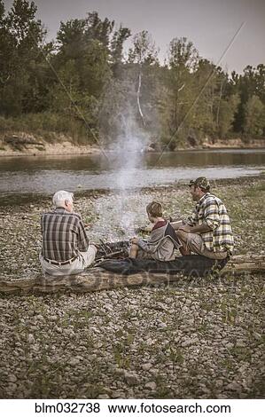 Stock Photo - Three generations of Caucasian men relaxing near campfire. Fotosearch