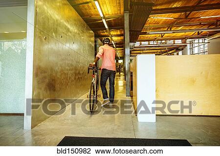 Stock Image - African American businessman pushing bicycle into office. Fotosearch