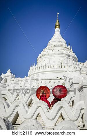 Stock Photograph - "Asian monks sitting under umbrellas at historic temple, Mingun, Mandala, Myanmar". Fotosearch