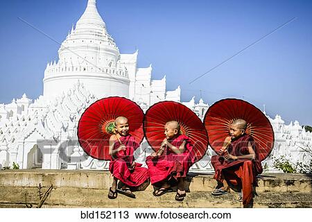 Stock Image - "Asian monks sitting under umbrellas near historic temple, Mingun, Mandala, Myanmar". Fotosearch