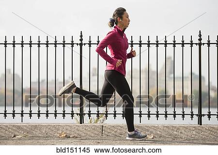 Stock Photography - Asian woman running on waterfront path. Fotosearch