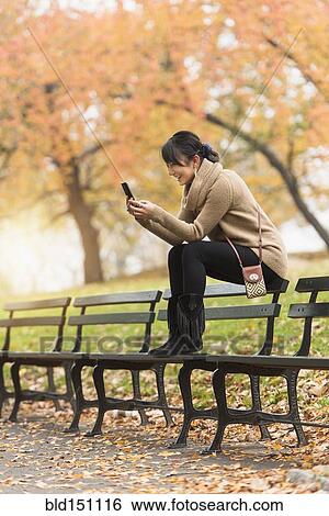 Stock Photograph - Asian woman using cell phone on park bench. Fotosearch