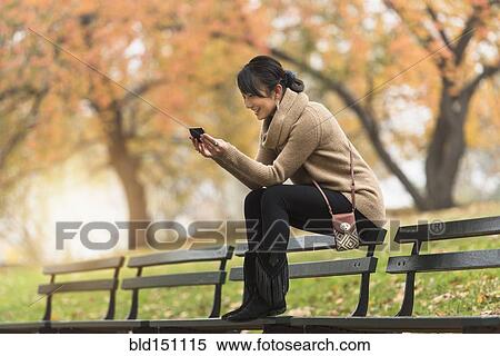 Asian woman using cell phone on park bench View Large Photo Image Stock Photography - Asian woman using cell phone on park bench. Fotosearch