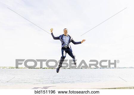 Stock Photograph - Black businessman jumping for joy at waterfront. Fotosearch