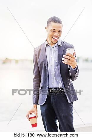 Stock Image - Black businessman using cell phone outdoors. Fotosearch