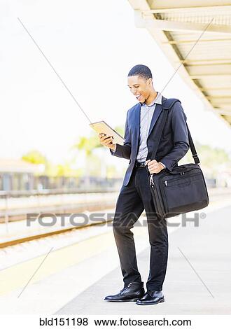 Stock Photo - Black businessman using digital tablet on train platform. Fotosearch