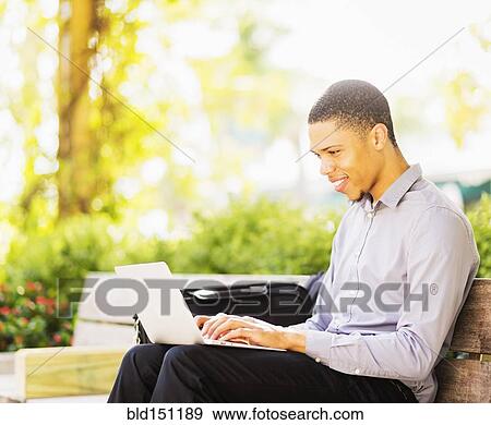 Stock Photo - Black businessman using laptop outdoors. Fotosearch