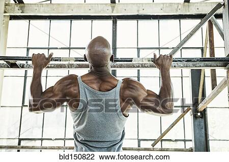 Stock Image - Black man doing pull-ups in warehouse. Fotosearch