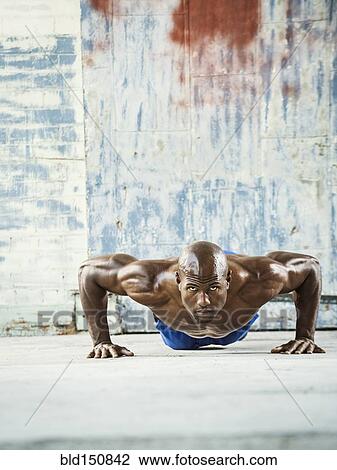 Stock Image - Black man doing push ups in warehouse. Fotosearch