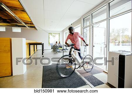 Stock Image - Blurred view of businessman pushing bicycle into office. Fotosearch