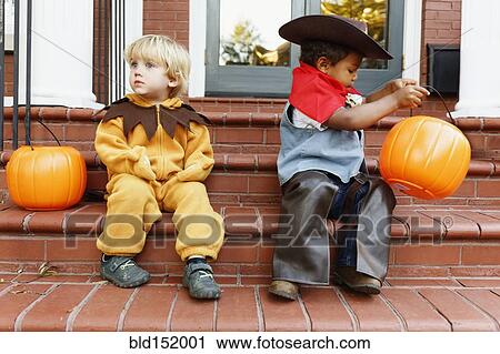 Stock Image - Boys in costumes trick sitting on front stoop on Halloween. Fotosearch