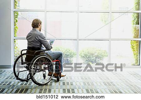 Stock Image - Businessman in wheelchair using digital tablet in office. Fotosearch