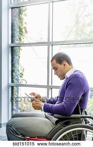 Stock Photography - Businessman in wheelchair using digital tablet in office. Fotosearch