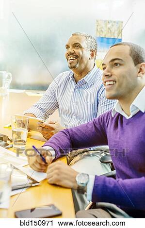 Stock Image - Businessmen laughing in office meeting. Fotosearch