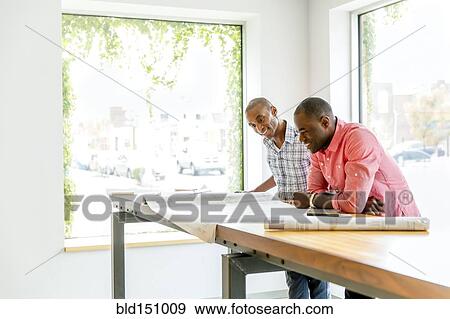 Stock Photo - Businessmen reading blueprints in office. Fotosearch