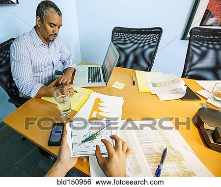 Businessmen working at conference table in office View Large Photo Image Stock Photograph - Businessmen working at conference table in office. Fotosearch