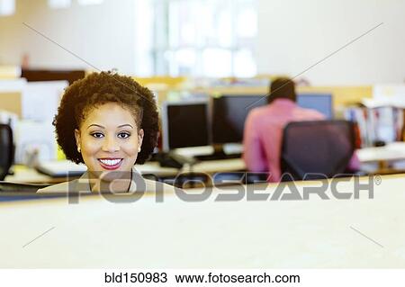 Stock Image - Businesswoman smiling at desk in office. Fotosearch