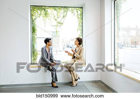 Stock Photo - Businesswomen talking in window of office lobby. Fotosearch