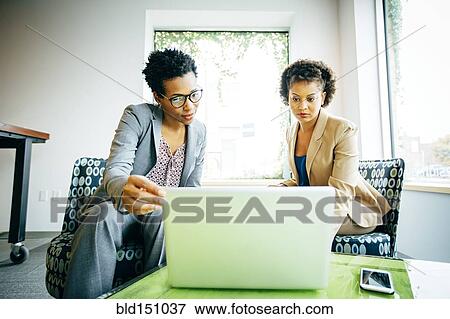 Stock Photo - Businesswomen using laptop in office lobby. Fotosearch