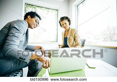 Businesswomen using laptop in office lobby View Large Photo Image Stock Photograph - Businesswomen using laptop in office lobby. Fotosearch