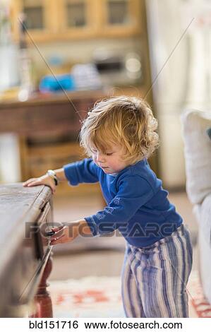 Stock Photograph - Caucasian baby opening coffee table drawers. Fotosearch