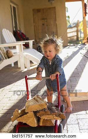 Stock Photo - Caucasian baby pushing firewood on toy cart. Fotosearch