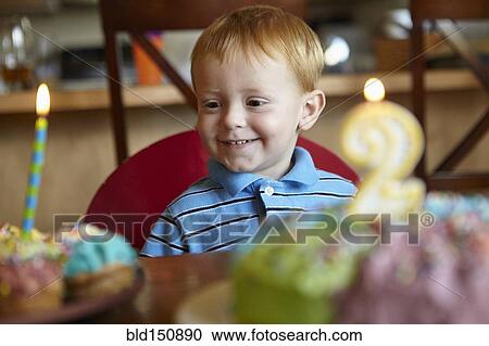Stock Image - Caucasian boy admiring birthday cake and cupcake. Fotosearch