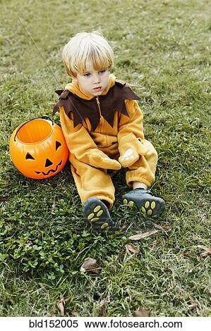 Stock Photography - Caucasian boy in lion costume sitting on grass on Halloween. Fotosearch