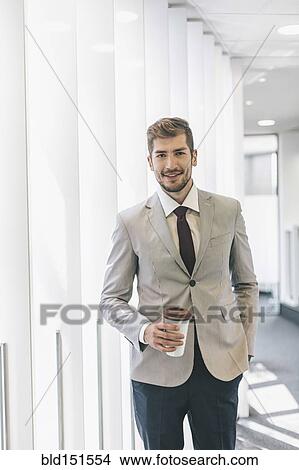 Picture - Caucasian businessman drinking coffee in office corridor. Fotosearch