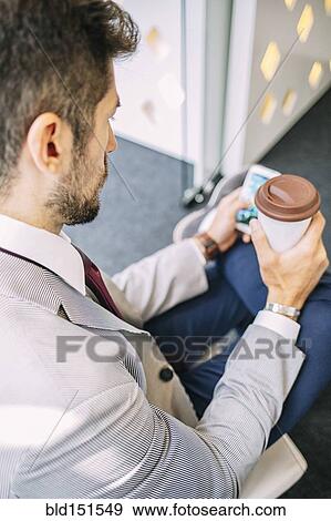 Stock Photo - Caucasian businessman drinking coffee and using cell phone. Fotosearch